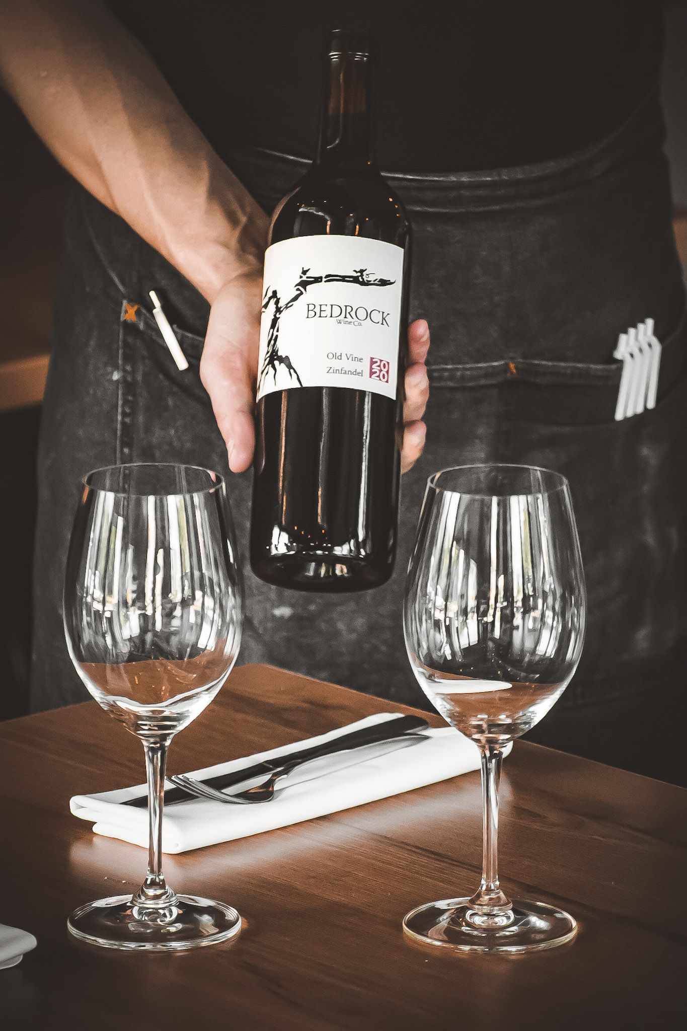 A person elegantly pours red wine into two crystal wine glasses, creating a festive atmosphere.