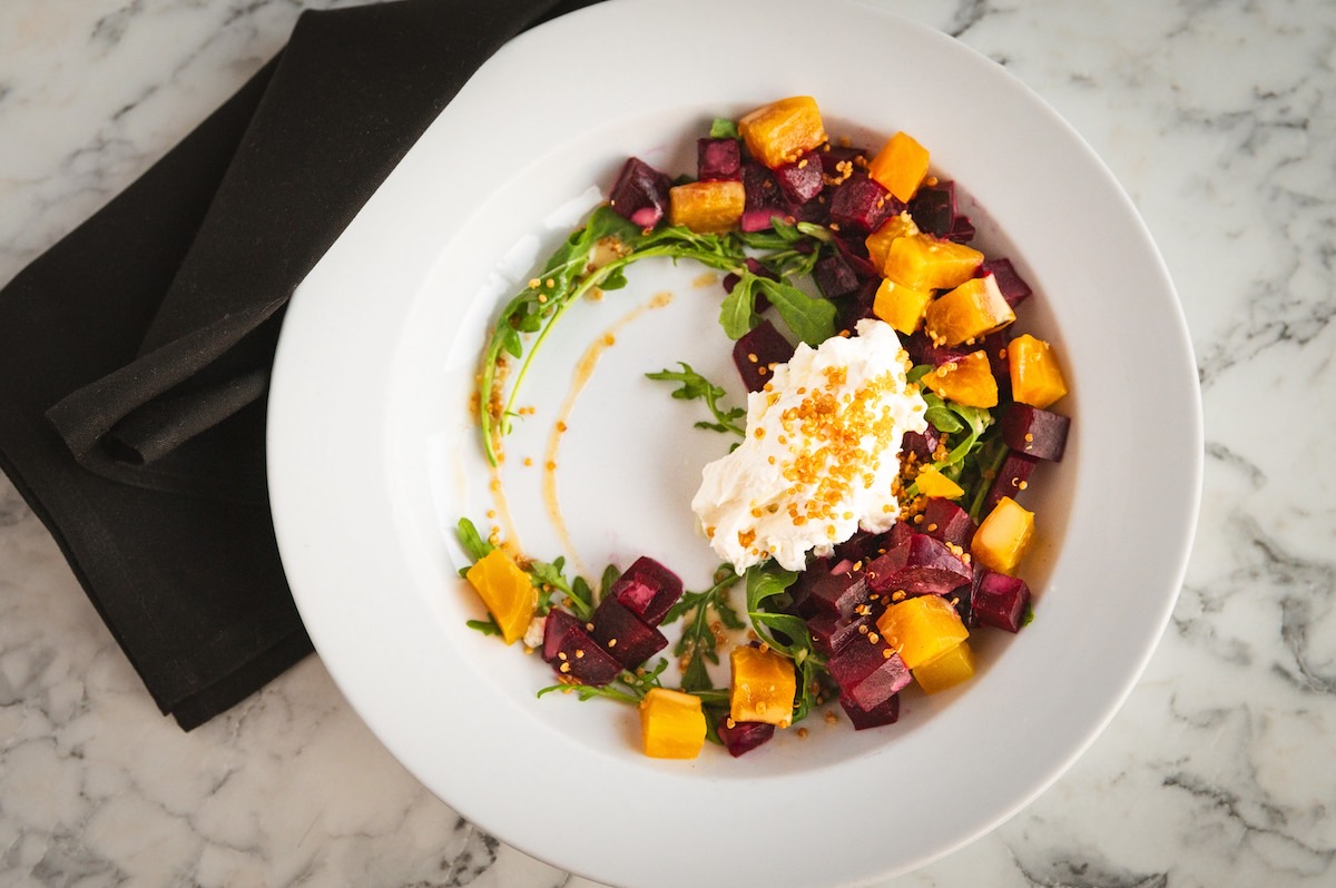 A white plate featuring a colorful salad accompanied by a silver spoon resting beside it.